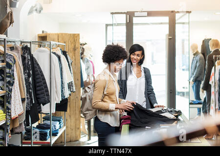 Friends talking while checking shirts at store on sunny day Stock Photo