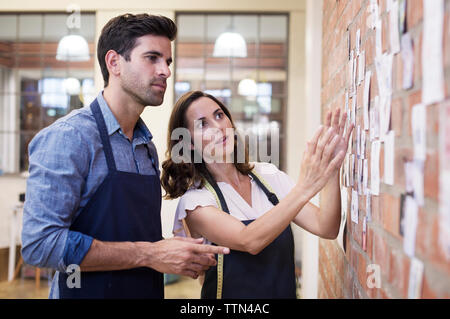 Fashion designer showing photographs on brick wall to colleague while working at workshop Stock Photo