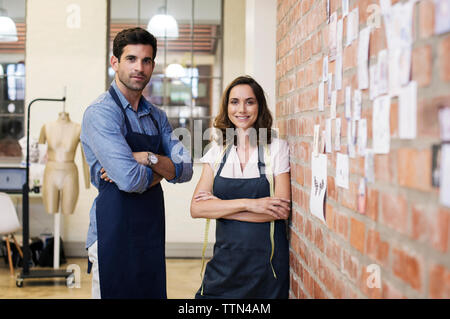 Portrait of confident fashion designers standing by brick wall at workshop Stock Photo