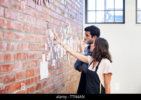Female fashion designer showing photographs on brick wall to male colleague while working at workshop Stock Photo