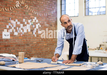 Male fashion designer looking away while working at table in workshop Stock Photo