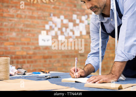 Male fashion designer writing while working at table in workshop Stock Photo