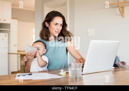 Woman feeding son while using laptop computer at table Stock Photo