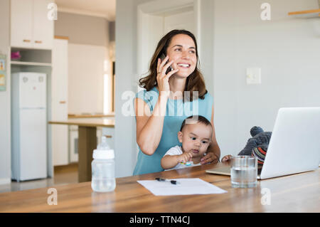 Woman talking on smart phone while sitting with son at home Stock Photo
