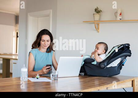 Baby boy sitting in seat looking at mother using smart phone Stock Photo