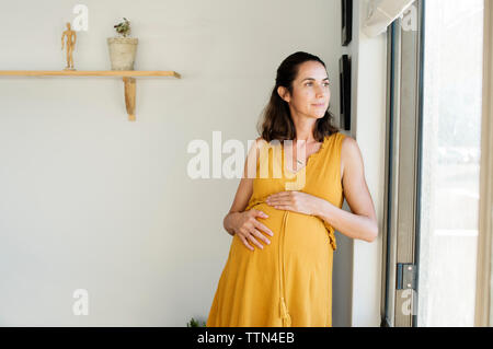 Thoughtful pregnant woman standing by window at home Stock Photo