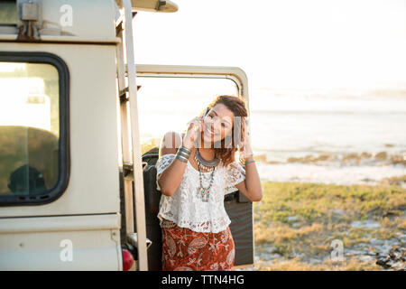 Happy woman talking on mobile phone by off-road vehicle at beach Stock Photo
