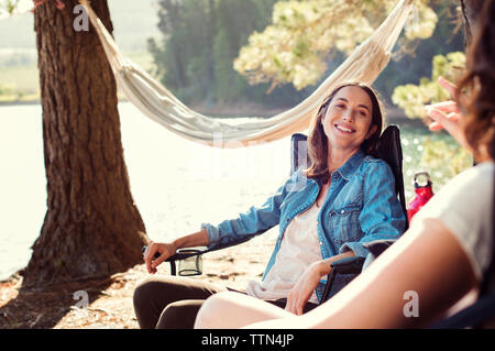Happy female friends relaxing on armchairs at lakeshore Stock Photo