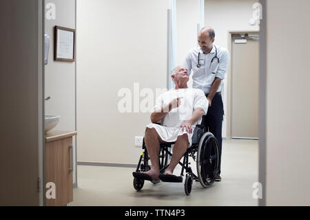 Doctor carrying patient on wheelchair in corridor Stock Photo