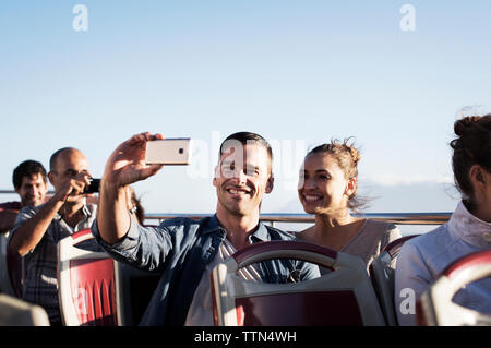 Couple taking selfie while traveling in double-decker bus against clear sky Stock Photo