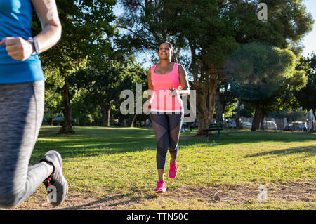 Female friends jogging on grassy field against trees in park Stock Photo