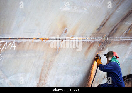 Side view of welder welding container ship at industry