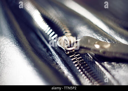 Metal zipper on a black leather bag reflects the sun's bright light Stock Photo