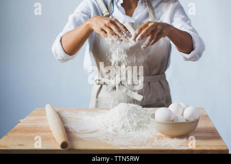 Midsection of woman kneading dough on table while standing against wall in kitchen Stock Photo