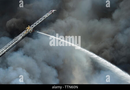Low angle view of firefighter on crane spraying water over gray smoke Stock Photo
