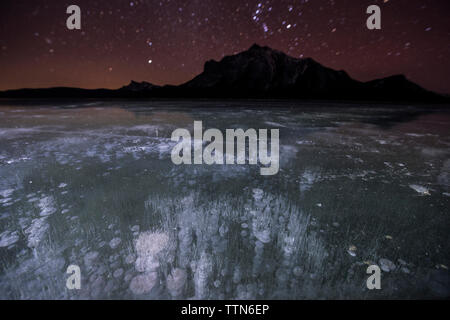 Majestic view of methane bubbles in Abraham Lake by mountains during night Stock Photo