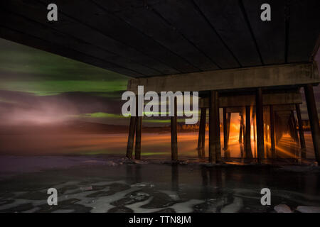 Low angle view of aurora borealis over sea with wooden pier in foreground Stock Photo