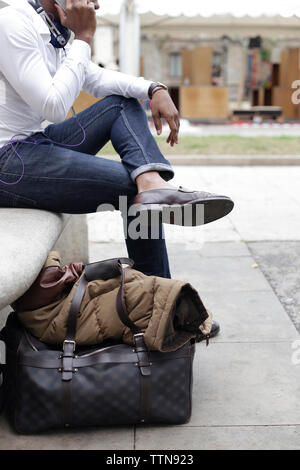 Low section of man using phone while sitting on seat by footpath in city Stock Photo