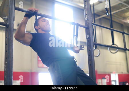 Confident male adaptive athlete screaming while doing chin-ups in gym Stock Photo