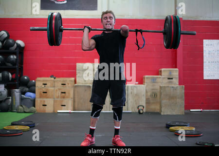 Confident male adaptive athlete lifting barbell while standing against wall in gym Stock Photo