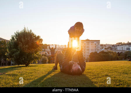 Playful father lifting daughter while lying on grassy field at park during sunny day Stock Photo