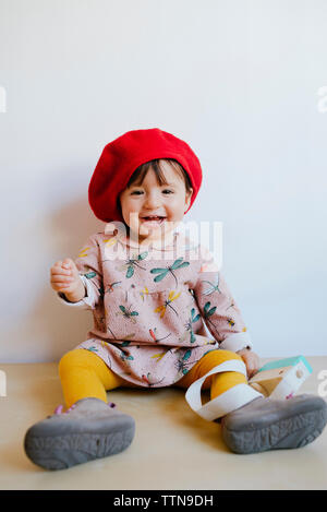 Portrait of cheerful baby girl wearing red hat sitting on floor against wall at home Stock Photo