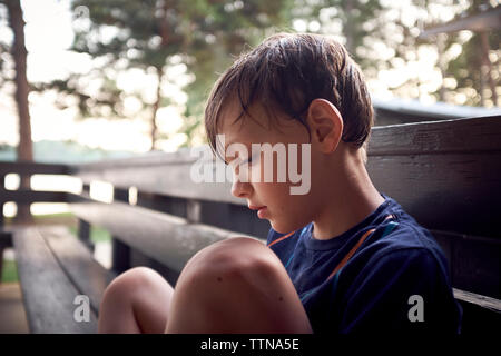 Thoughtful boy sitting on bench at park Stock Photo
