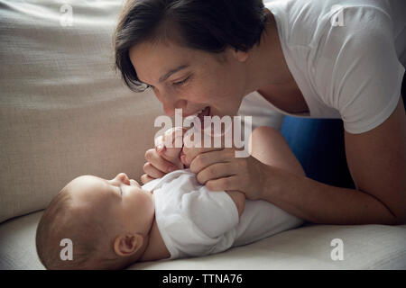 Happy mother playing with son lying on sofa at home Stock Photo