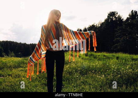 Relaxed woman wearing poncho while standing on grassy field Stock Photo