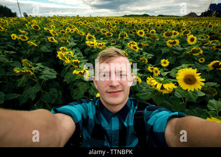 High angle portrait of man winking eye while standing amidst sunflowers growing at farm Stock Photo