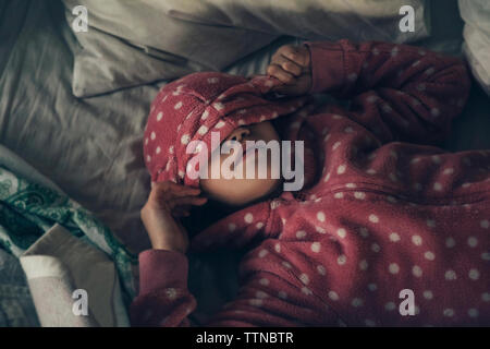 High angle view of girl wearing pink hooded jacket while lying on bed at home Stock Photo