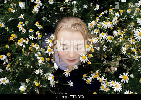 High angle view of woman with eyes closes sitting amidst daisies on field in park