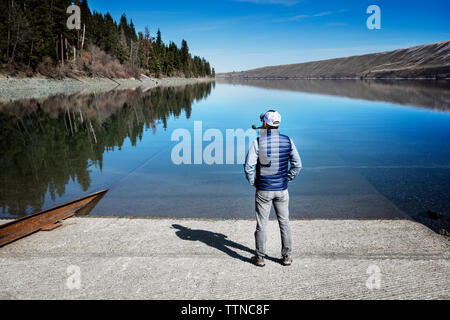 Rear view of mature man smoking pipe while standing at lakeshore Stock Photo