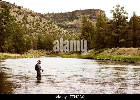 Premium Photo  An elderly man kneels at the edge of a riverbank He wears a fishing  hat and vest and holds a fishing rod