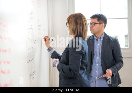 businesswoman explaining to make colleague while writing on whiteboard in office Stock Photo