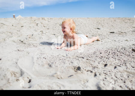 Blonde caucasian toddler smiling on sand dune in her diaper Stock Photo
