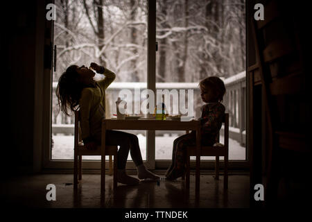 Sisters eating in front of window with snowy view Stock Photo