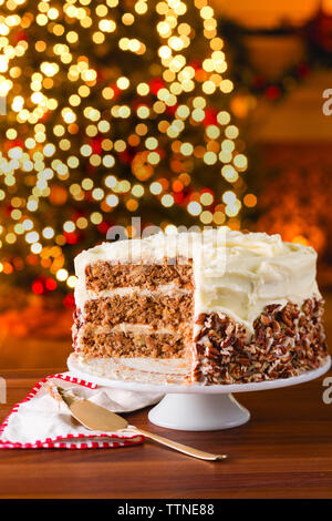 Cake on wooden table against illuminated Christmas tree at home Stock Photo