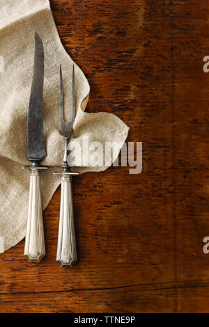 Overhead view of fork with kitchen knife and napkin on wooden table Stock Photo