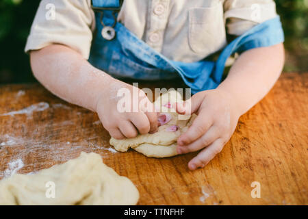 Midsection of boy kneading dough on wooden table at yard Stock Photo