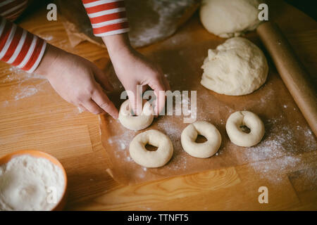 Cropped hands of woman preparing donuts on wooden table at home Stock Photo