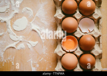 High angle view of eggs in carton by flour on wooden table in kitchen Stock Photo