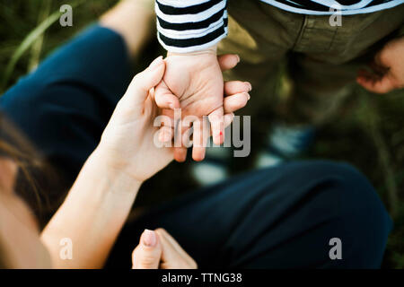 Mother holding child's hands outdoors with green background Stock Photo