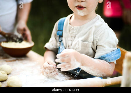 Midsection of boy kneading dough on wooden table at yard Stock Photo