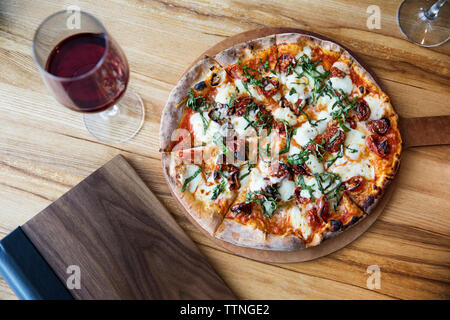 Overhead view of fresh pizza with red wineglass on restaurant table Stock Photo
