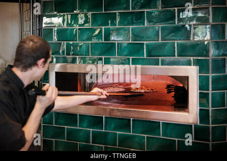 Side view of male chef placing pizzas in oven at commercial kitchen Stock Photo