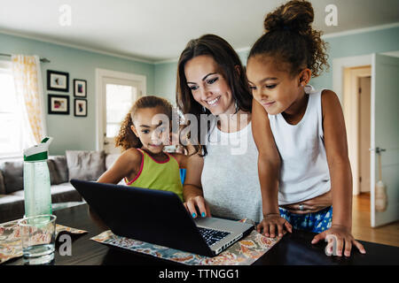 Happy woman using laptop with daughters at home Stock Photo