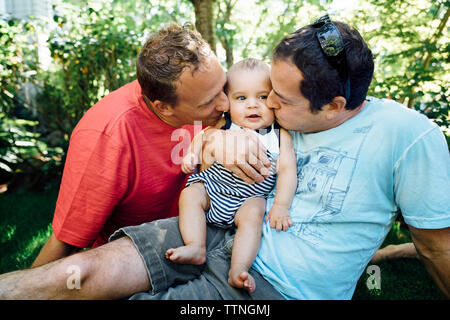 Homosexual couple kissing baby while sitting in backyard Stock Photo