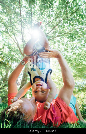 Father holding baby upside down while lying in backyard Stock Photo