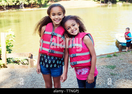 Portrait of girls wearing life jackets while standing at lakeshore Stock Photo
